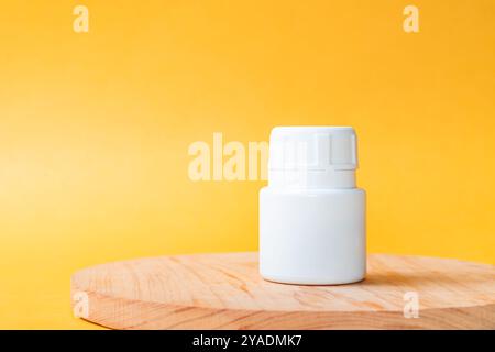 Eine weiße Kunststoffflasche mit Schraubverschluss auf einer Holzoberfläche vor einem hellgelben Hintergrund. Die Flasche ist leer und hat ein einfaches Design Stockfoto