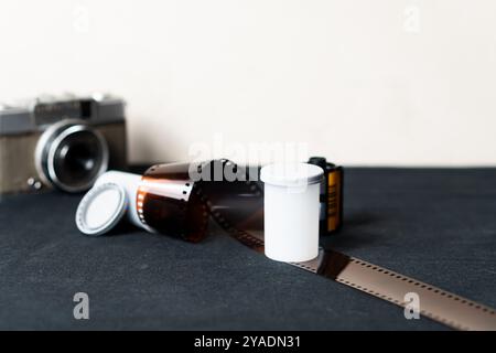 Eine Vintage-Kamera mit einer Rolle Film und einem weißen Filmkanister auf einer dunklen Oberfläche. Die Kamera ist im Hintergrund leicht unscharf, während die Fil Stockfoto