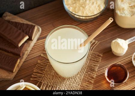 Frisches Molkenproteingetränk in einem Glasbecher mit ökologischem Bambusstroh mit Molkenproteinriegeln und Pulver Stockfoto