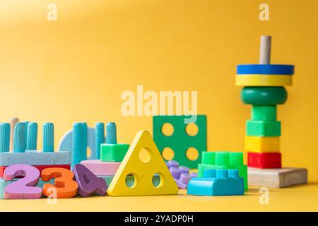 Ein farbenfrohes Arrangement von lehrreichen Spielzeugen, einschließlich Zahlenblöcken, geometrischen Formen und Stapelringen auf einem hellgelben Hintergrund. Die Spielzeuge sind m Stockfoto