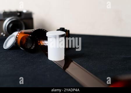 Eine Vintage-Kamera mit einer Rolle Film und einem weißen Filmkanister auf einer dunklen Oberfläche. Die Kamera ist im Hintergrund leicht unscharf, während die Fil Stockfoto