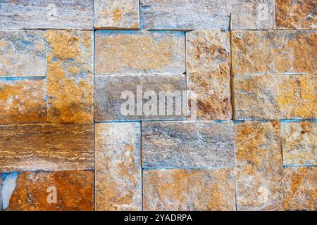 Nahaufnahme der strukturierten Steinmauer mit verschiedenen Braun-, Orange- und Grautönen. Stockfoto