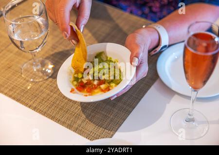 Nahaufnahme einer Person, die Chips in Guacamole taucht, mit einem Glas Wein und Wasser auf dem Tisch. Mexiko. Stockfoto