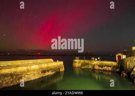 Rote aurorastrahlen und SAR-Bogen über dem Hafen von Coliemore vom geomagnetischen G4-Sturm im Oktober 2024 Stockfoto