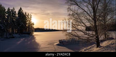 Ein ruhiger Winteruntergang über einem gefrorenen See, umgeben von einer atemberaubenden schneebedeckten Landschaft Stockfoto