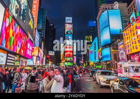 Touristen, die bei Nacht Selfies am Times Square machen, umgeben von hellen Plakatwänden, Verkehr und lebhaften Lichtern der Stadt. New York. USA. Stockfoto