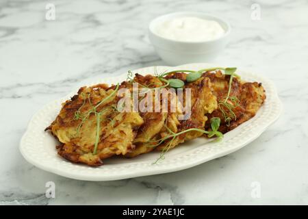 Köstliche Kartoffelpfannkuchen mit frischem Mikrogrün und Sauerrahm auf weißem Marmortisch, Nahaufnahme Stockfoto