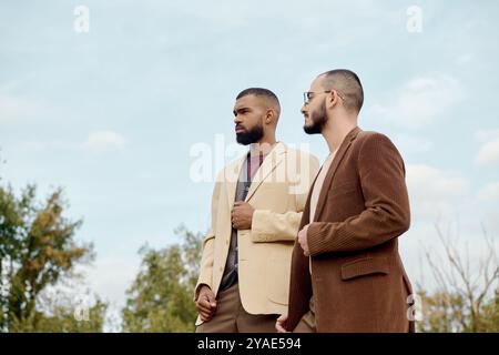 Zwei männliche Modelle zeigen trendige Herbstoutfits und stehen selbstbewusst auf einem malerischen Feld. Stockfoto