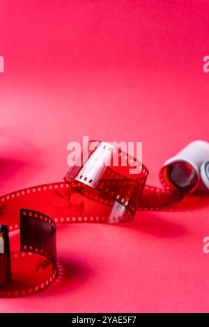 Eine Nahaufnahme eines roten Filmstreifens auf einem leuchtend rosa Hintergrund. Die Folie weist Perforationen entlang der Kanten auf und ist teilweise unberührt, creatin Stockfoto