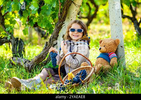 Das Kind untersucht die Trauben im Weinberg, das süße Mädchen schaut sich die Weinrebe in der Weinfarm an. Glückliches Kind spaziert im Sommer auf der Plantage. Das Konzept des Weinbergs Stockfoto