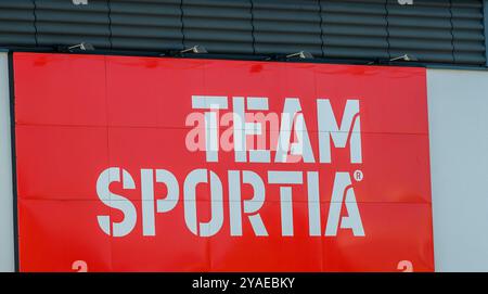 Ein auffälliges, leuchtend rotes Ladenschild kündigt Team Sportia an und zieht Käufer in einem lebhaften Einzelhandelsumfeld voller Aktivität und Energie an Stockfoto