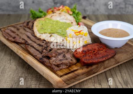 Gegrilltes Carne-Asada-Fleisch-Abendessen mit Reis, Chorizo und Bohnen auf einer Holzplatte. Stockfoto