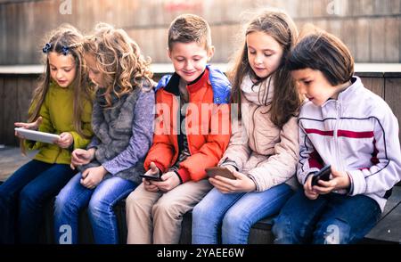 Kinder, die auf der Straßenbank im Park auf Smartphones spielen Stockfoto