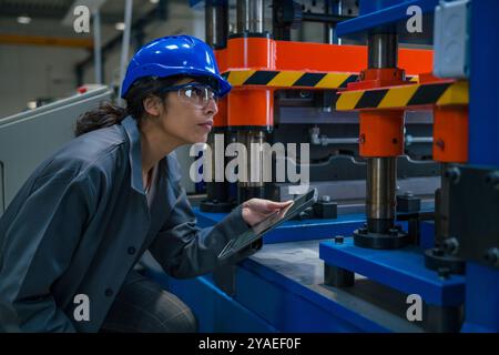 Indische Industrieingenieurin, mit blauem Helm und Schutzbrille, während einer Maschinenkontrolle in der Fabrik, Nahaufnahme. Wartungskonzept. Stockfoto