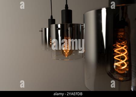 Eine moderne Lampe in einem dunklen Raum. Nahaufnahme der hängenden beleuchteten Glühlampen. Stockfoto