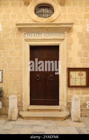 Dunkelbraune Holztür. Türklopfer. Verzierung. Rundes-Fenster. Kalkstein. antik. Mdina. Malta. Dunkelbraune Holztür. Türklopfer. Verzierung. Antik Stockfoto