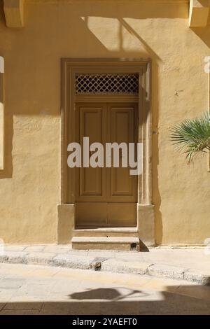 Beige gelbe Holztür. Beige gelbe Holztür. Türklopfer. Türklopfer. Gold. nobel. Gelbe Wand. gelbe Wand. Mdina. Malta. Glänzend. Eisengitter. Stockfoto