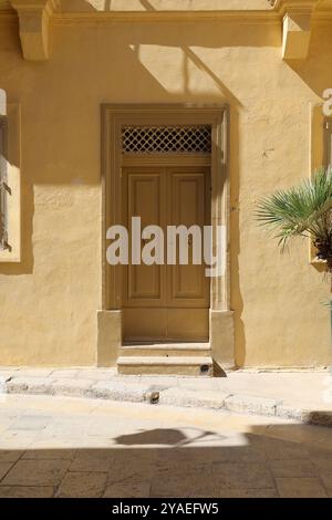 Beige gelbe Holztür. Beige gelbe Holztür. Türklopfer. Türklopfer. Gold. nobel. Gelbe Wand. gelbe Wand. Mdina. Malta. Glänzend. Eisengitter. Stockfoto