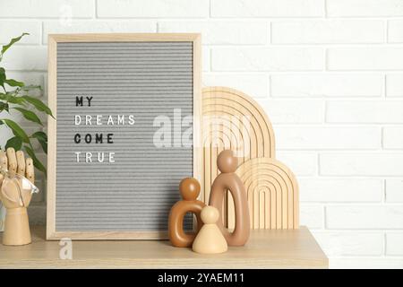 Brieftafel mit dem Satz My Dreams Come True, Pflanzen- und Dekorationselemente auf Holztisch in der Nähe der weißen Ziegelwand Stockfoto