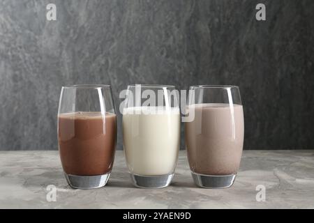 Köstliche Proteinshakes in Gläsern auf grauem, strukturiertem Tisch Stockfoto