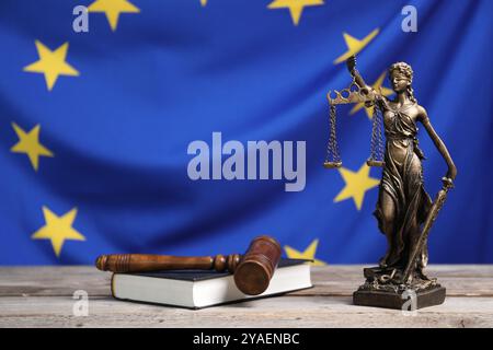 Figur der Justizfrau, richterlicher Hammer und Buch auf Holztisch vor der Flagge der Europäischen Union Stockfoto