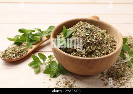 Getrockneter Oregano in Schüssel, Löffel und grüne Blätter auf Holztisch, Nahaufnahme Stockfoto