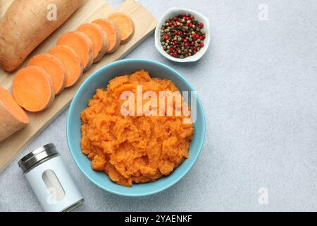 Leckere Süßkartoffelpüree in der Schüssel, frisches Gemüse und Gewürze auf grauem Tisch, flache Ladefläche. Leerzeichen für Text Stockfoto