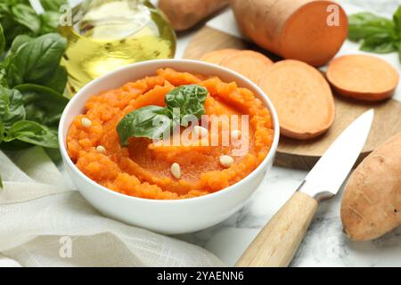 Leckere Süßkartoffelpüree mit Basilikum, Samen in der Schüssel und Zutaten auf dem Tisch, Nahaufnahme Stockfoto