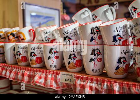 Colmar, Frankreich - 5. Juni 2023: Keramikbecher mit traditionellen elsässischen Motiven, Störche, Kugel und Brezeln in einem Souvenirladen Stockfoto