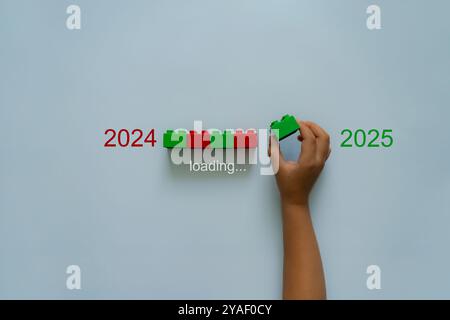 Laden von Neujahr 2024 bis 2025 mit Kinderhand, die grünen Kunststoffblock in Progress-Leiste steckt. Starten Sie das neue Jahr 2025 mit Zielplan, Zielkonzept und Strategie. Stockfoto