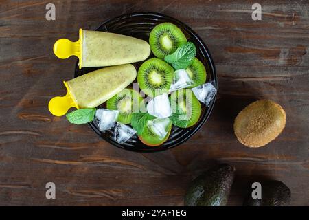 Hausgemachtes gesundes Sorbet (Fruchteis) aus Avocado und Kiwi auf dem schwarzen Teller zwischen Kiwi-Stücken, Minzblättern, Eiswürfeln auf dem alten rustikalen Stockfoto