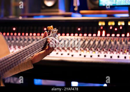 Der Interpret singt einen Track auf seiner Elektro-Akustikgitarre im professionellen Studio, mischt und meistert Melodien, um neue Musik zu produzieren. Talentierter Künstler komponiert Lieder mit Bedienpult. Nahaufnahme. Stockfoto