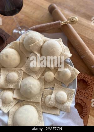 Frisch zubereitete Ravioli, die auf einem Teller neben einem Holzrollstift und einem Ravioli-Cutter liegen, bereit für den nächsten Schritt in der Nudelherstellung Stockfoto