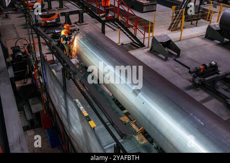 Arbeiter reinigt Schweißnähte an Stahlrohren mit Schleifmaschine. Stockfoto