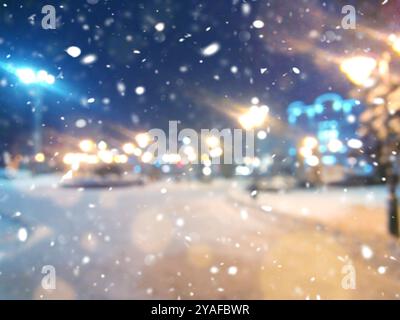 Unscharfer Hintergrund. Stadtblick, Lichter, fallender Schnee, Nacht, Straße, Bokeh-Spots von Scheinwerfern Autos. Urbane Kulisse Winterlandschaft der Straße in der Stadt AT Stockfoto