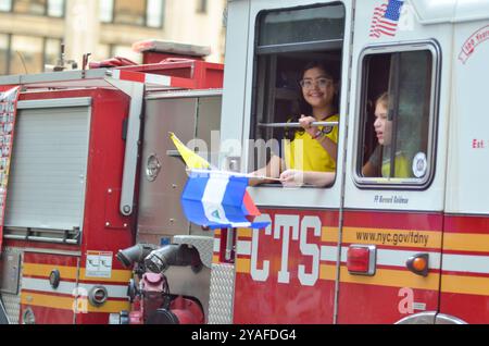 New York, New York, USA. Oktober 2024. Junge Teilnehmer, die Flaggen von einem FDNY-Feuerwehrwagen schwenken, bei der Hispanic Day Parade entlang der Sixth Avenue in New York City. (Kreditbild: © Ryan Rahman/Pacific Press via ZUMA Press Wire) NUR REDAKTIONELLE VERWENDUNG! Nicht für kommerzielle ZWECKE! Quelle: ZUMA Press, Inc./Alamy Live News Stockfoto