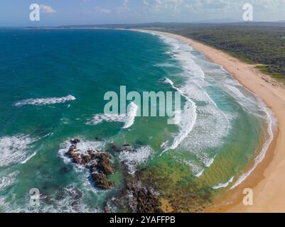 Aus der Vogelperspektive auf einen felsigen Ausläufer am Ende eines langen Sandstrandes bei Bermagui in New South Wales, Australien Stockfoto