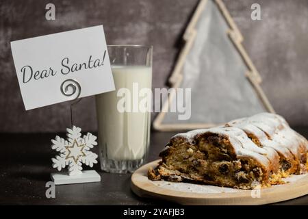 Papiernotiz mit Nachricht LIEBER WEIHNACHTSMANN hausgemachte Weihnachten traditionelle Kuchen Kuchen mit Marzipannüssen und getrockneten Früchten Gebäck Dessert Stollen mit Glas Milch für WEIHNACHTSMANN. Winterferien saisonale Atmosphäre. Köstliche geschmackvolle Komposition Tischeinstellung Kopierraum Stockfoto