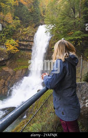 Eine Frau steht an einem Geländer und schaut auf einen großen Wasserfall im Herbstwald, Brienzersee, Giessbach Wasserfall, Schweiz, Europa Stockfoto