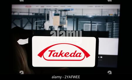 Deutschland. August 2024. In dieser Abbildung hält eine Person ein Handy mit dem Logo des japanischen Unternehmens Takeda Pharmaceutical Company Limited vor der Webseite. Quelle: SOPA Images Limited/Alamy Live News Stockfoto