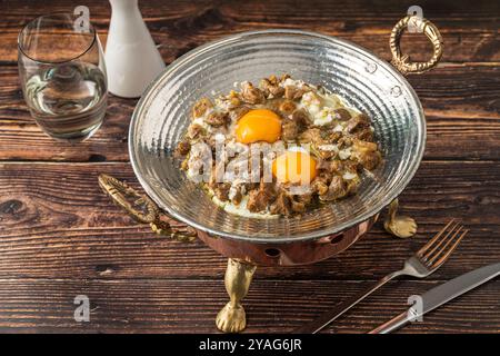 Eier mit Fleisch, gebraten in einer Kupferpfanne auf einem Holztisch. Türkischer Name kavurmali yumurta Stockfoto