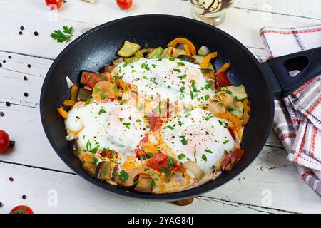 Shakshuka in einer Pfanne. Spiegeleier mit Tomaten, Pfeffer, Zucchini und Kräutern Stockfoto