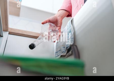 Mann wirft Plastikflasche in den Recyclingbehälter. Sortieren von Abfällen nach Material in farbigen Abfallbehältern in der Küche. Stockfoto