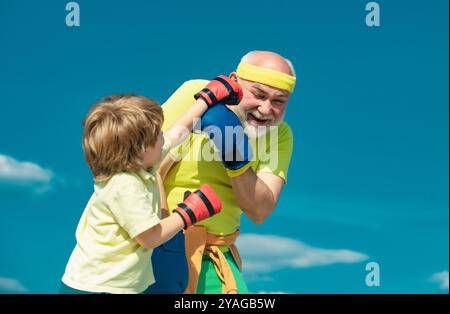 Gesunder Kämpfergroßvater und Enkel mit Boxhandschuhen. Ein älterer Mann schlägt einen Boxsack. Schöner älterer Mann, der Boxtritte übt. Stockfoto