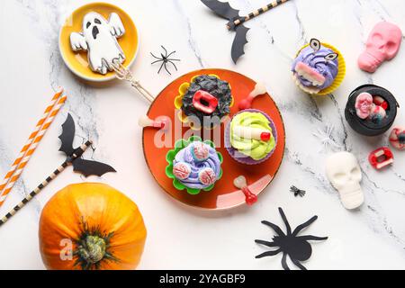 Komposition mit köstlichen Halloween Cupcakes, Süßigkeiten und Strohhalmen auf hellem Hintergrund Stockfoto