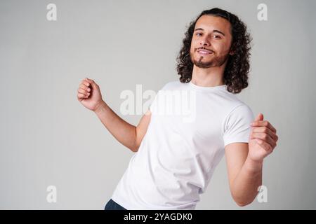Fröhlicher Mann mit lockigen Haaren, der im Studio im lässigen Outfit fröhlich feiert Stockfoto