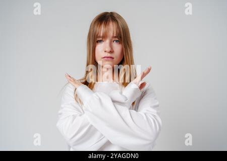 Junge Frau mit langen Haaren posiert selbstbewusst mit überkreuzten Armen vor einem schlichten Hintergrund Stockfoto