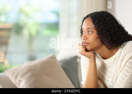 Schwarze Frau, die durch ein Fenster schaut, sitzt auf einem Sofa in einem Haus Stockfoto