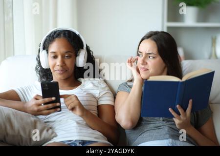 Porträt eines Buchlesers in Vorderansicht, der sich verärgert hat, weil ihr Freund zu Hause Musik hört Stockfoto