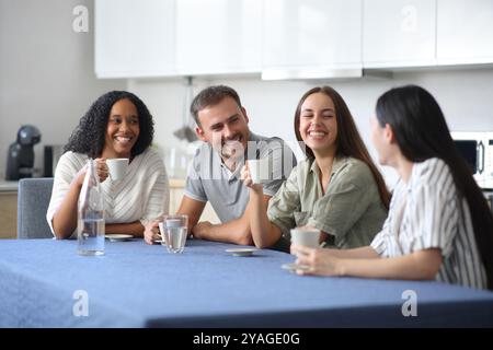 Glückliche Freunde, die sich in der Küche unterhalten und zu Hause Kaffee und Wasser trinken Stockfoto